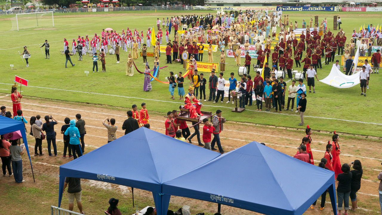 Looking down on the school parade, A boy dressed in ornate robes sitting on a throne is being carried along the running track.
