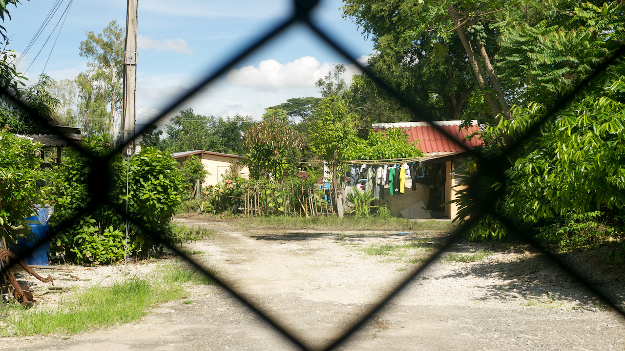 View through a chain link fence at our second host family's place at the little group of houses.